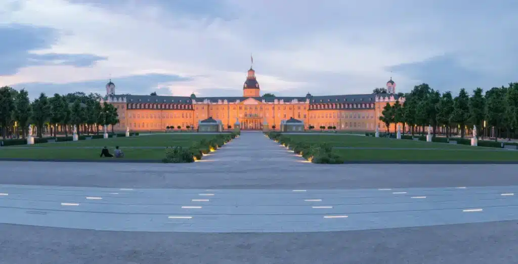 Panoramablick auf das Schloss Karlsruhe , umgeben von symmetrischen Gärten und einem Weg in der Abenddämmerung.