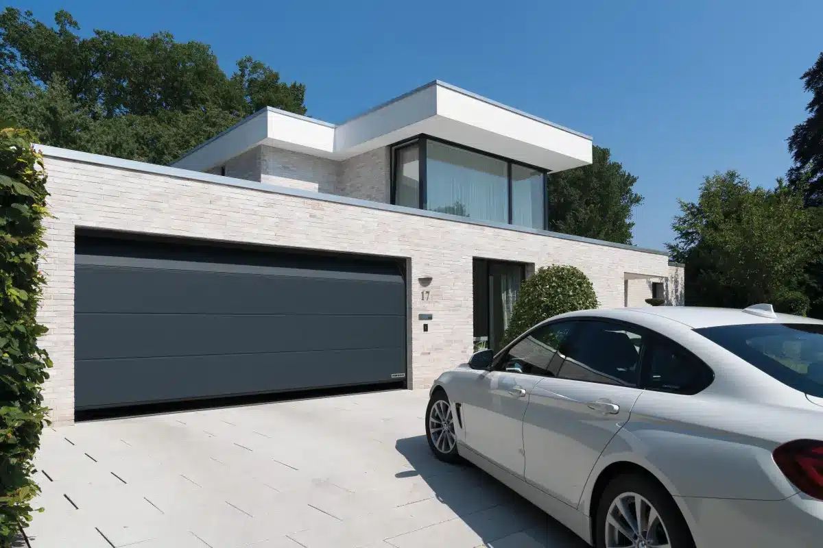 Modernes Haus mit Flachdach, großen Fenstern und angebauter Garage. In der Einfahrt parkt ein weißes Auto.