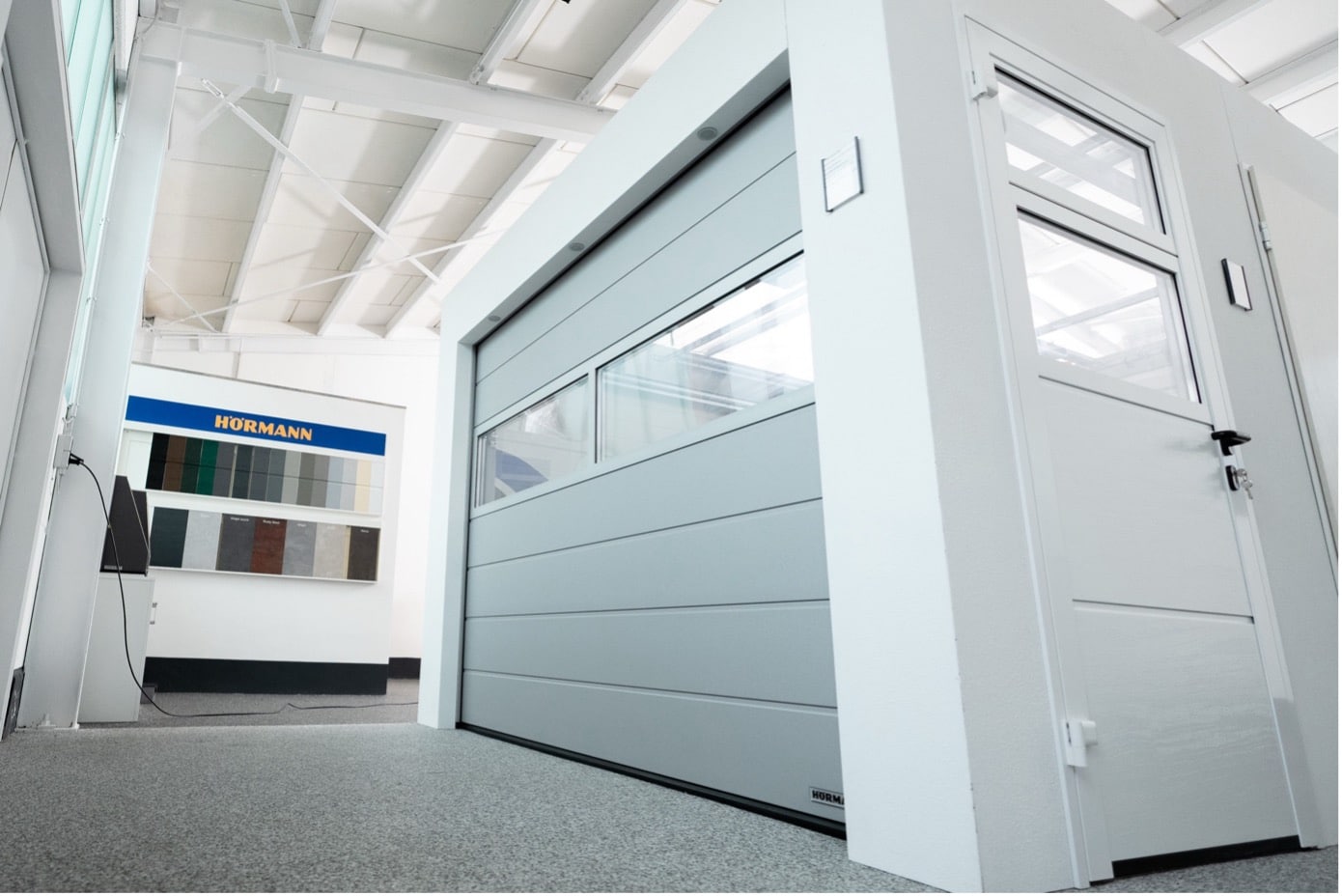 Moderner Ausstellungsraum mit einem grauen Garagentor, einer weißen Tür und Farbmustern an der Wand.
